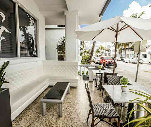 En utomhusservering med vita möbler och parasoller i ett stadsmiljö. (AI-genererad text)