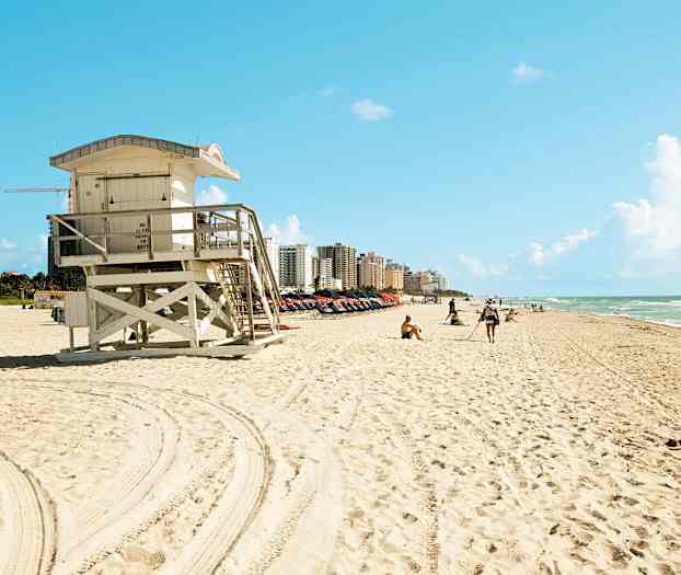 En strand med ett livvakttorn i förgrunden och byggnader i bakgrunden. (AI-genererad text)