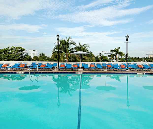 En stor utomhuspool med solstolar och parasoller vid kanten, omgiven av palmer. (AI-genererad text)