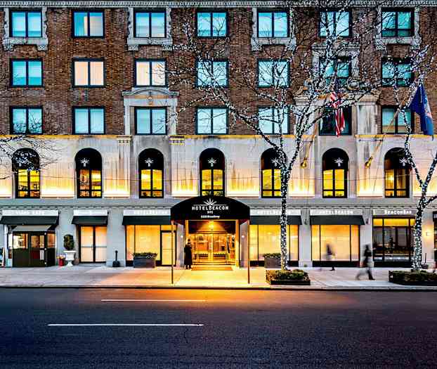 Hotellbyggnad vid en gata, med entré markerad som Hotel Beacon, omgiven av cafémiljö och ljusslingor i träden. (AI-genererad text)