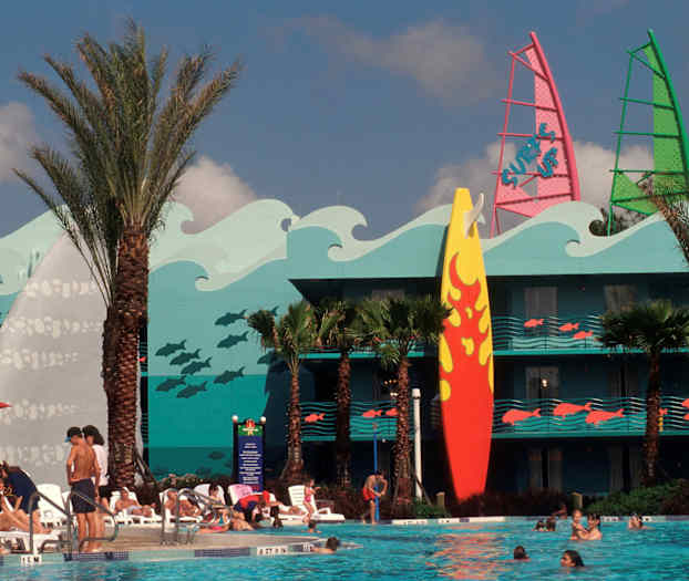 En pool omgiven av solstolar och människor. Bakom finns en byggnad med färgglad dekoration av vågor, fiskar och en stor surfbräda. (AI-genererad text)