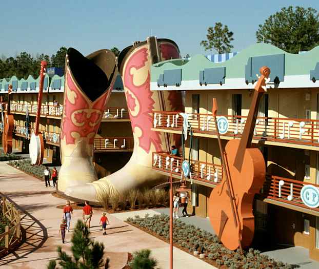 Ett färgglatt hotellkomplex med stora cowboyboots och en gitarr i dekor. Folk promenerar på gångvägen. (AI-genererad text)