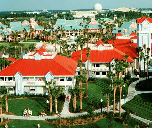 Bild av en resort med byggnader med röda tak och ljusblå fasader, palmträd och gångvägar. (AI-genererad text)