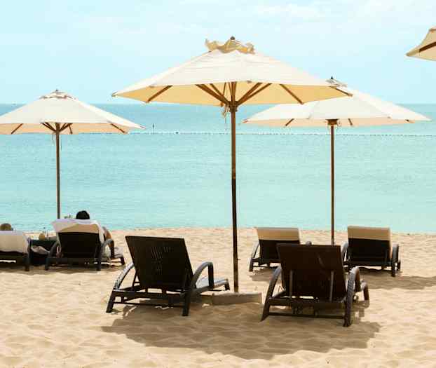 Sandstrand med solstolar och parasoller vid vattnet. (AI-genererad text)