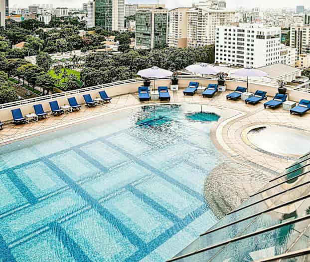 En utomhuspool med blå solstolar och parasoller på ett soldäck, och stadslandskap i bakgrunden. (AI-genererad text)