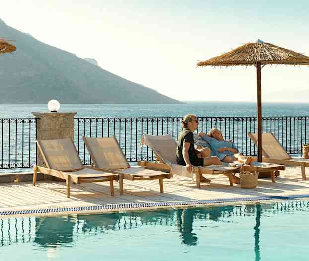 Solstolar vid en pool med utsikt över havet och berg i bakgrunden. (AI-genererad text)