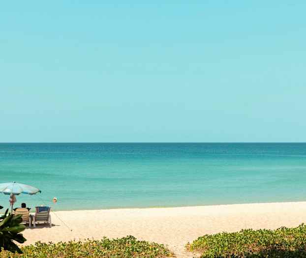 En sandstrand med paraply och solstolar bredvid havet. (AI-genererad text)