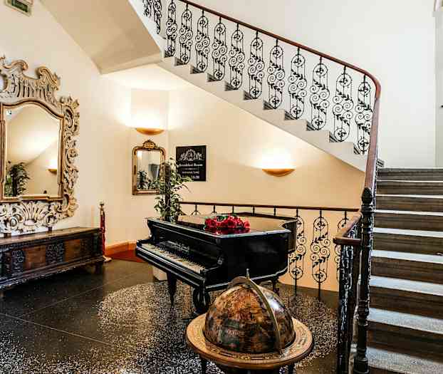 En trappa med smidesräcken, en glasglob, en svart flygel med röda blommor på, samt en dekorativ spegel. (AI-genererad text)