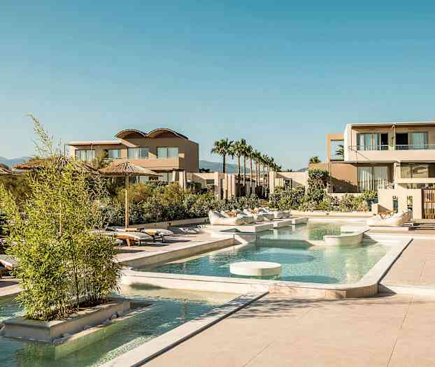 En lyxig resort med pool, solstolar och moderna byggnader under en klar himmel. (AI-genererad text)