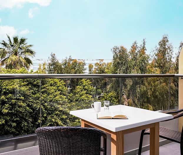 Bild av en terrass med ett bord och två stolar samt utsikt över träd och blå himmel. (AI-genererad text)