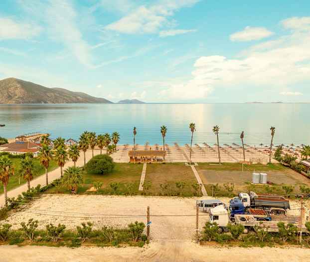 Utsikt över en strand med parasoller och palmer, en del av byggnader och fordon syns också. (AI-genererad text)