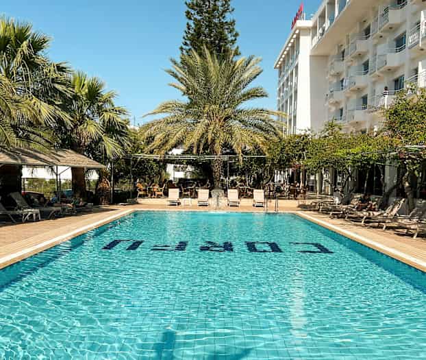 Utomhuspool med solstolar och palmer, mot en hotellbyggnad. (AI-genererad text)