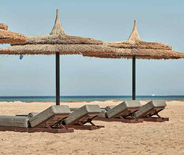 Solstolar med halmtak på sandstrand med hav i bakgrunden. (AI-genererad text)