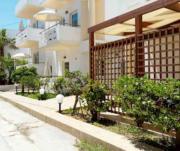 En gata med vita byggnader, gröna buskar och parasoller. (AI-genererad text)