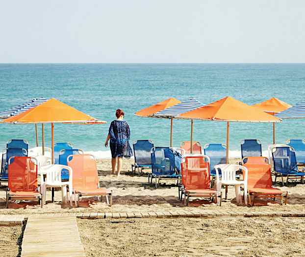 Strand med solstolar och parasoller, en person går mot havet. (AI-genererad text)