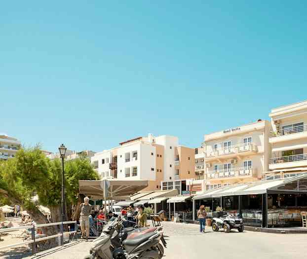 Bild av en gata med restauranger och motorcyklar framför byggnader i ett soligt område. (AI-genererad text)