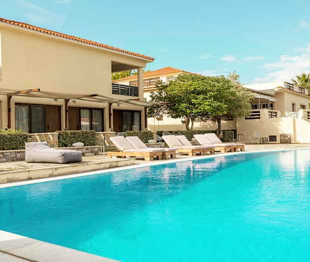 Utomhuspool framför byggnader med solstolar och omgivande växtlighet. (AI-genererad text)