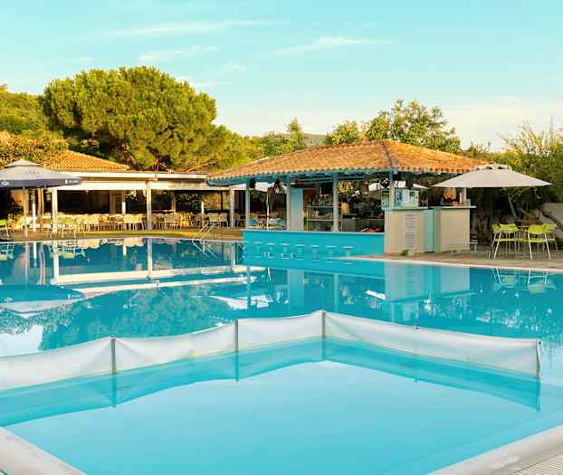 En utomhuspool med barstolar i vattnet, omgiven av bord och stolar samt grönska. (AI-genererad text)