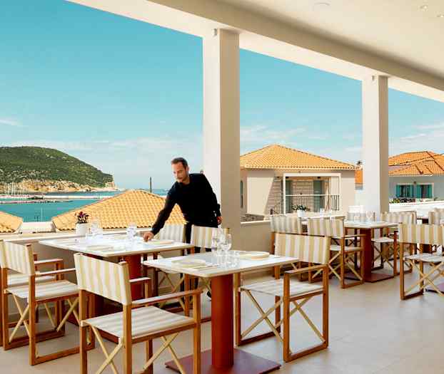 Restaurang med bordsuppsättning, utsikt över havet och terrass, mot bakgrund av terrakottatak och en grönskande bergskulle. (AI-genererad text)