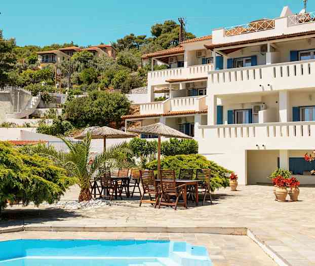 Vit byggnad med balkonger, grönskande trädgård och pool i förgrunden. (AI-genererad text)