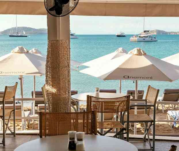 Utsikt från en terrass mot stranden med solstolar, parasoller och havet i bakgrunden. (AI-genererad text)