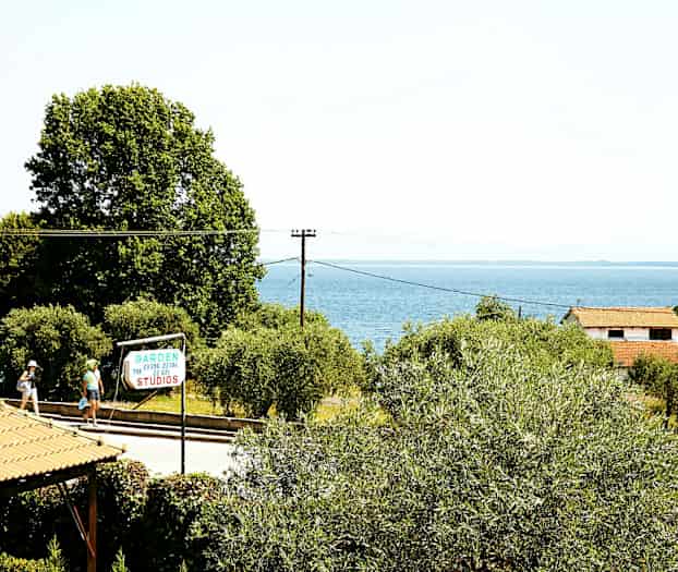 Utsikt över havet med grönskande träd, ett hus med rött tak och en skylt för Garden Studios. (AI-genererad text)