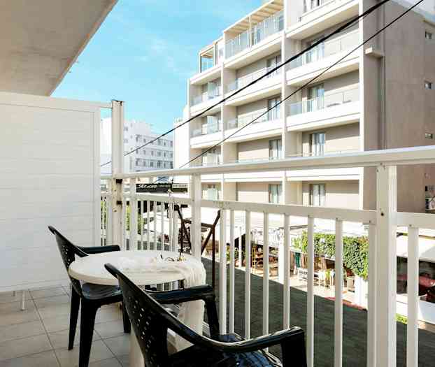 En balkong med två stolar och ett bord, utsikt mot byggnader. (AI-genererad text)