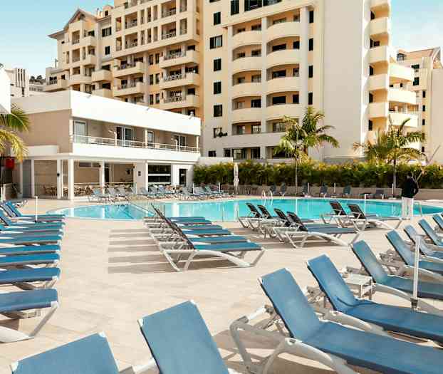 Utomhuspool med solstolar och omgivande byggnader. (AI-genererad text)