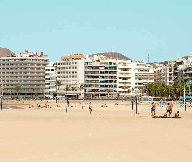 Strand med sand och människor som solar och spelar volleyboll framför flera höghus. (AI-genererad text)