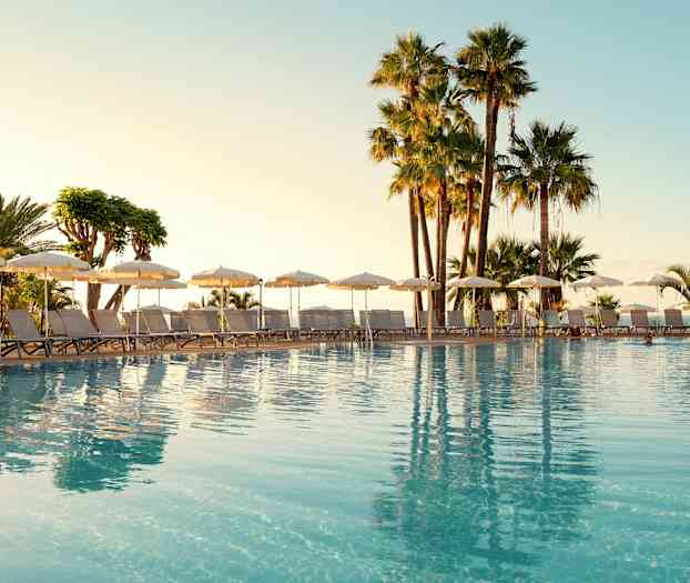 Utomhuspool med solstolar och parasoller, omgiven av palmer. (AI-genererad text)