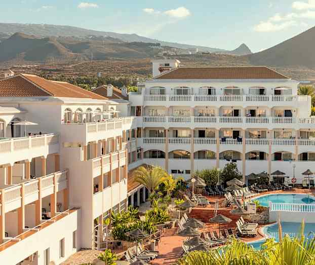 Hotellbyggnad med poolområde och solstolar, omgiven av berglandskap. (AI-genererad text)