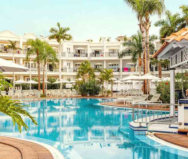 Bild av ett hotell med en pool, omgiven av solstolar, parasoller och grönska. (AI-genererad text)