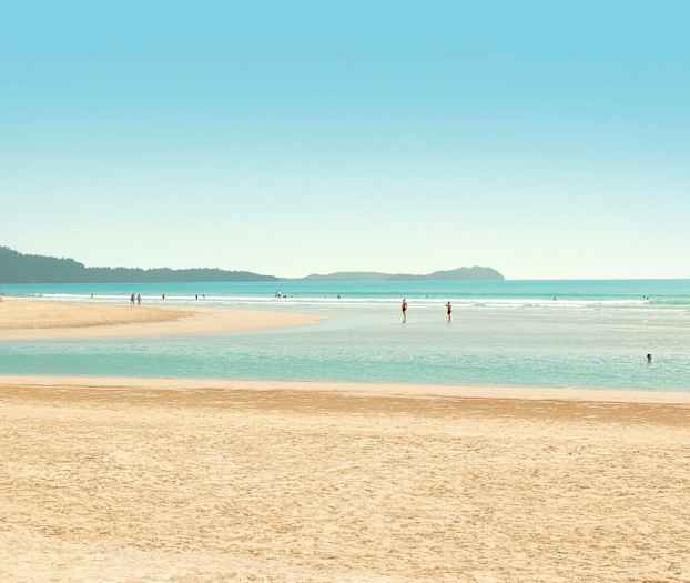 En strand med människor som badar och promenerar i vattnet. (AI-genererad text)