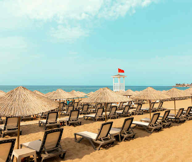 Strand med solstolar och parasoller, samt en livräddartorn med röd flagga. (AI-genererad text)