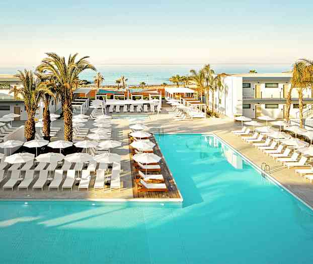 En hotellpool omgiven av solstolar och parasoller, med palmer och en havsutsikt i bakgrunden. (AI-genererad text)