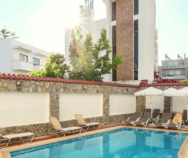 En mindre utomhuspool omgiven av solstolar och byggnader. (AI-genererad text)