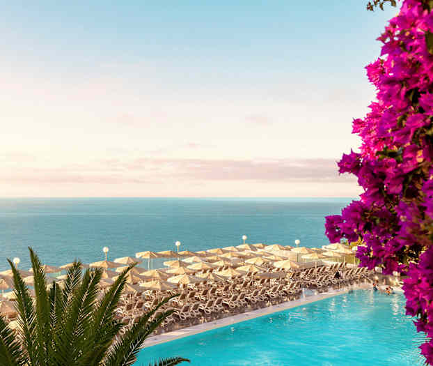 Solstolar med parasoller vid en pool med utsikt över havet och blommor. (AI-genererad text)