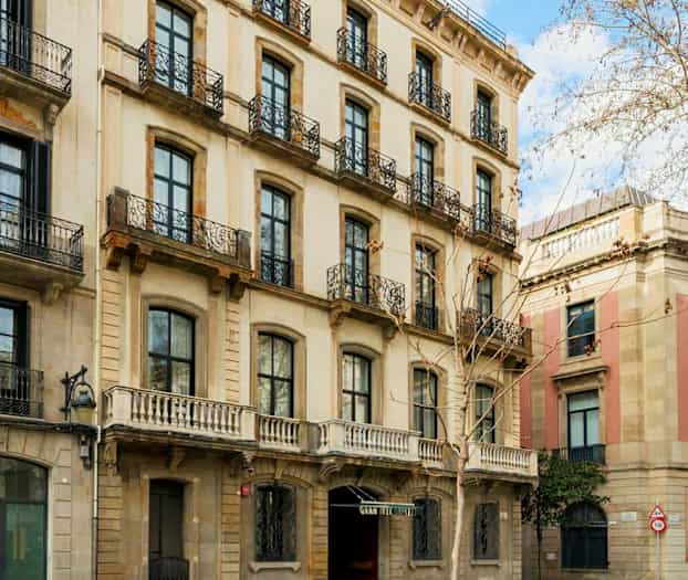 Fasad av en byggnad med flera våningar och järnbalkonger, belägen vid en gata med träd och trottoar. (AI-genererad text)