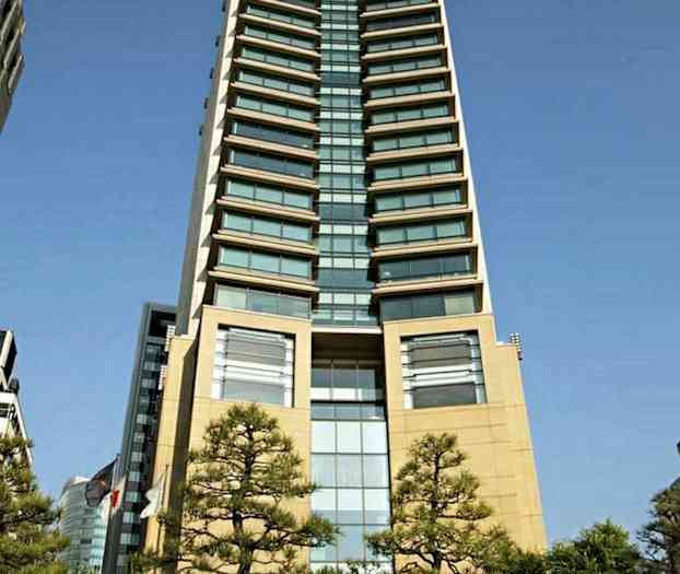 En hög byggnad fotograferad underifrån med träd i förgrunden och en skylt med texten "The Peninsula" framför. (AI-genererad text)