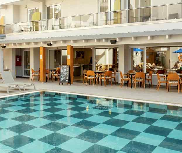 Utomhuspool med rutigt bottenmönster framför hotellbyggnad med balkonger och restaurang. (AI-genererad text)