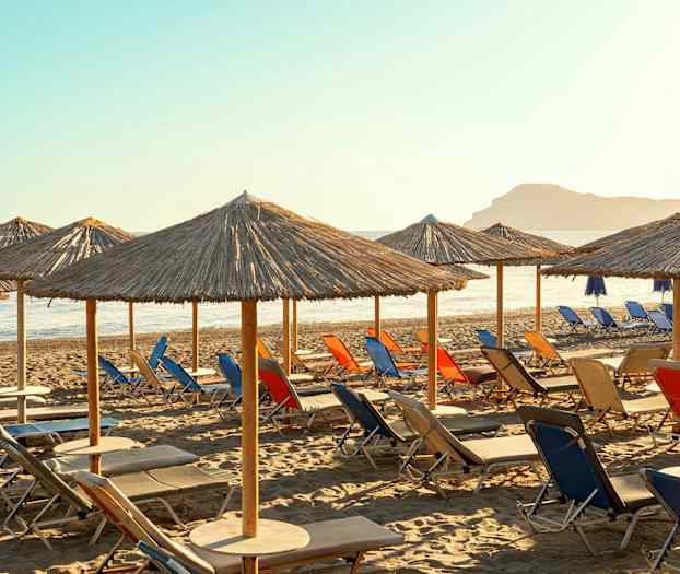 Strand med solstolar och halmparasoller under klar himmel. (AI-genererad text)