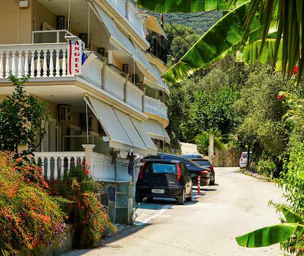 En byggnad med balkonger och markiser vid en väg med parkerade bilar och grönska. (AI-genererad text)