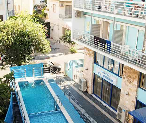 En swimmingpool med blå vatten omgiven av staket, belägen vid ett hotell med blå fasad. (AI-genererad text)