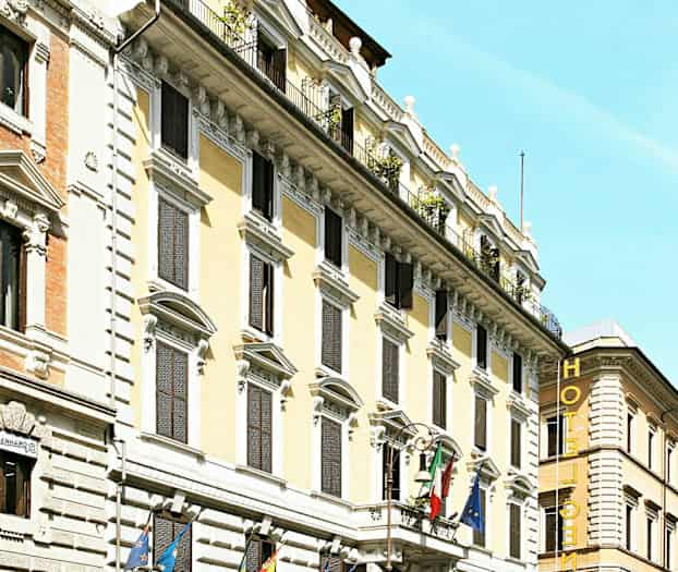 Fasad av ett hotell med flera våningar, dekorerad med flaggor och omgiven av bilar och motorcyklar. (AI-genererad text)