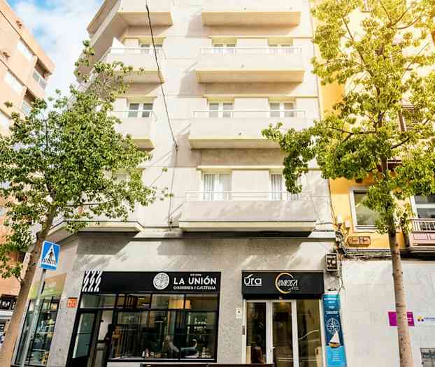 Flerfamiljshus med balkonger, butikslokaler på bottenplan och viss grönska runtom. (AI-genererad text)