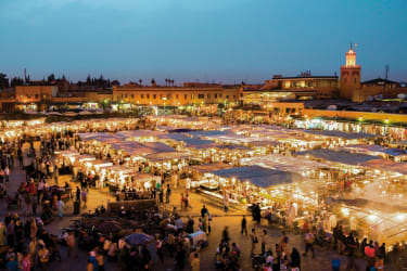 Torget Jemaa el Fna i Marrakech i skymningen, där ett vimmel av människor rör sig runt bland de belysta matstånden.