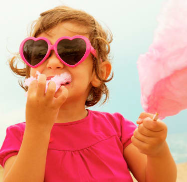 En flicka klädd i rosa och med hjärtformade solglasögon äter sockervadd.