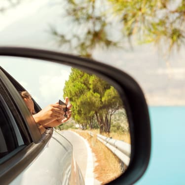 I backspegel på en bil syns en person som lutar sig ut och fotar med mobilen.