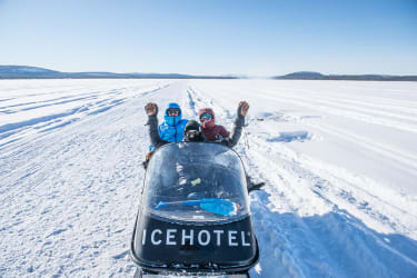 Tre personer åker på en snöscooter från Icehotel