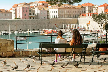 Två kvinnor sitter på en bänk och tittar mot Dubrovniks gamla stad.